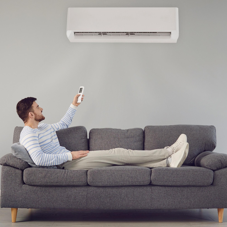 Homme détendu sur un canapé, réglant la climatisation avec une télécommande.