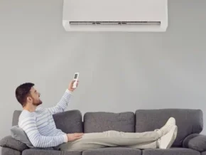 Homme détendu sur un canapé, tenant une télécommande pour un climatiseur.